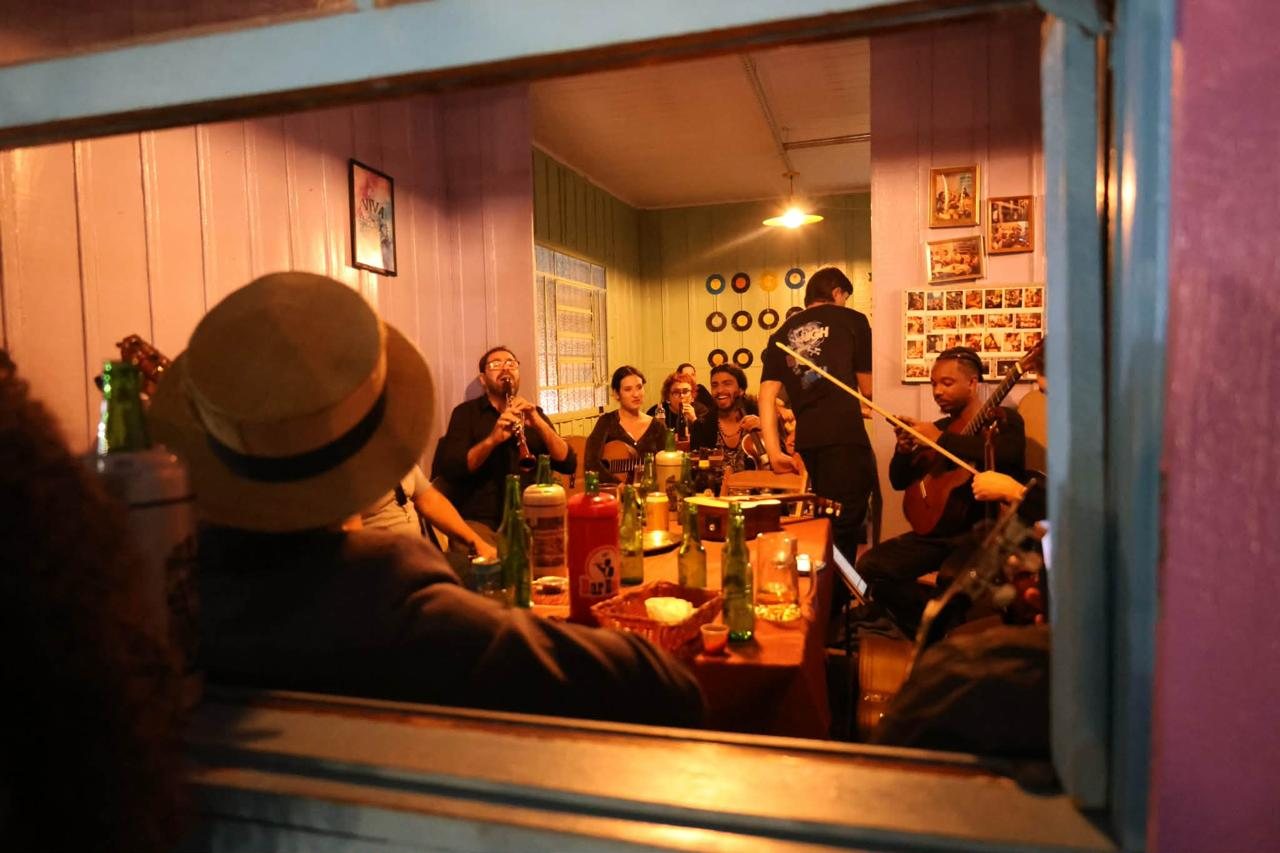 Roda de choro vista pela janela de um bar, com o clarinetista Alexandre Ribeiro ao fundo